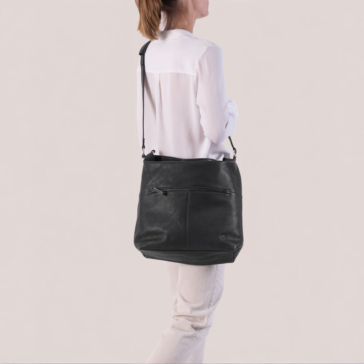 Eine elegante, schwarze Beuteltasche mit Schulterriemen, getragen von einer Person in heller Kleidung. Die Tasche hat ein minimalistisches Design und wirkt modern und funktional.