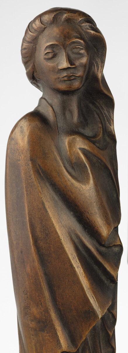 Die Skulptur 'Frau im Wind' von Ernst Barlach aus dem Jahr 1931 zeigt eine abstrakte Frauenfigur aus Bronze in expressionistischem Stil, mit geschlossenen Augen und drapiertem Gewand. Die Oberfläche der Skulptur hat eine braune, kupferfarbene Patina.