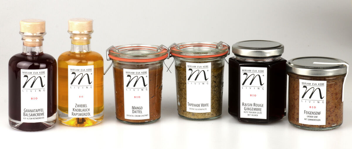 Das ZEIT-Jubiläums-Set »Herzhaft« enthält sechs verschiedene Bio-Feinkost-Produkte in Gläsern und Flaschen: Granatapfel-Balsamessig, Zwiebel-Knoblauch-Würzöl, Mango-Chutney, Gourmet-Würzmischung, Rotweinessig und Feigenmarmelade. Die Gläser haben rote oder schwarze Schraubdeckel und die Flaschen haben Holzkorken. Die Produkte stehen nebeneinander vor einem neutralen Hintergrund.