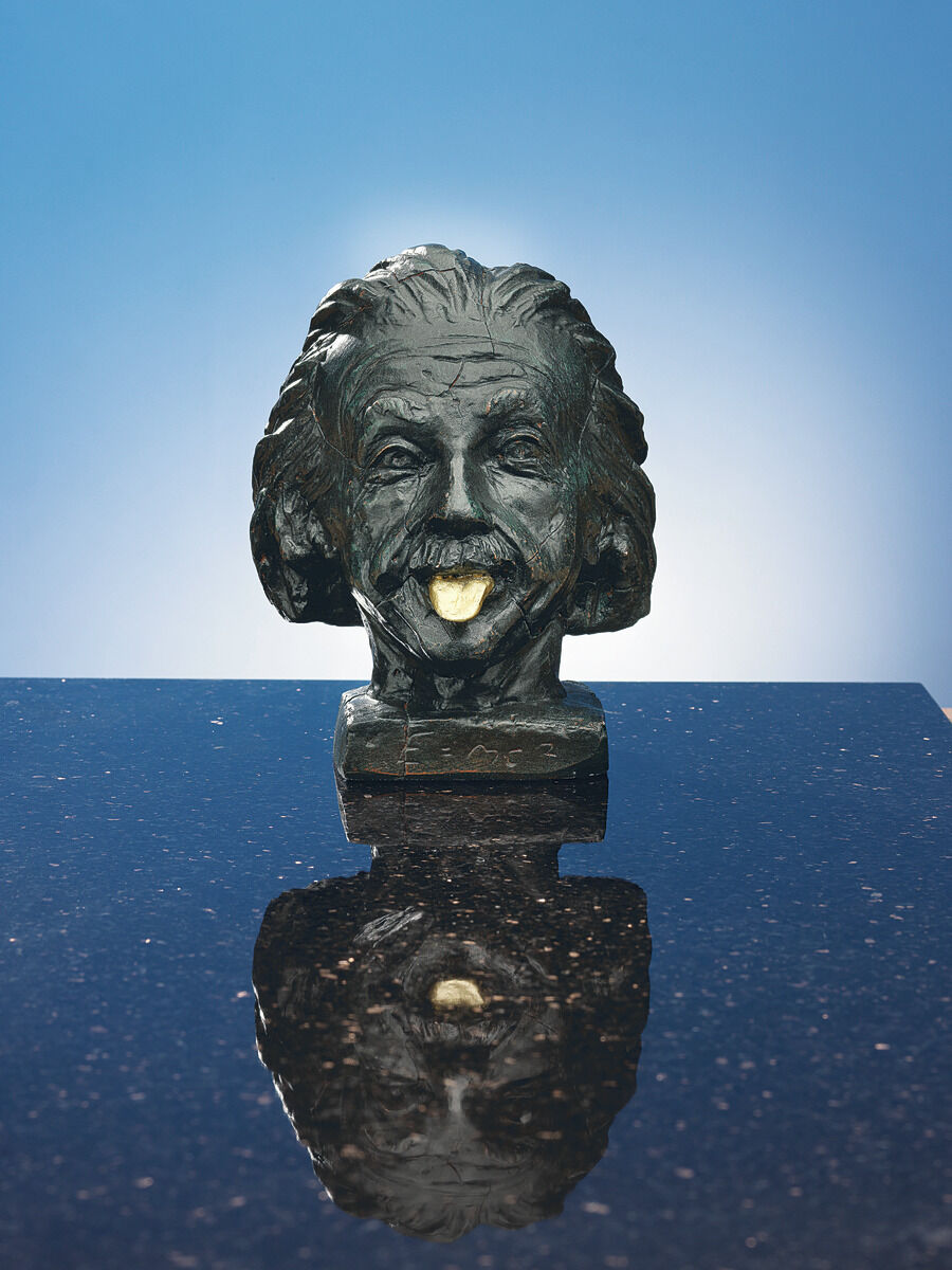 Büste von Albert Einstein mit einer goldenen Zunge auf einer reflektierenden schwarzen Oberfläche vor einem blauen Hintergrund.