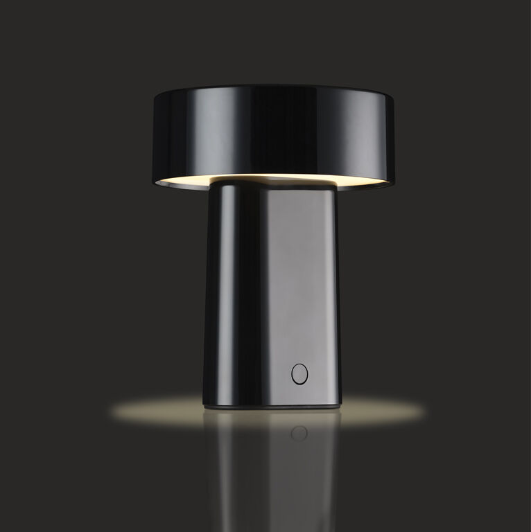 Eine moderne, tragbare Tischlampe mit breitem, schwarzem Lampenschirm und minimalistischem Design steht auf dunklem Hintergrund. Die Lampe leuchtet nach unten und schafft ein weiches, warmes Licht.