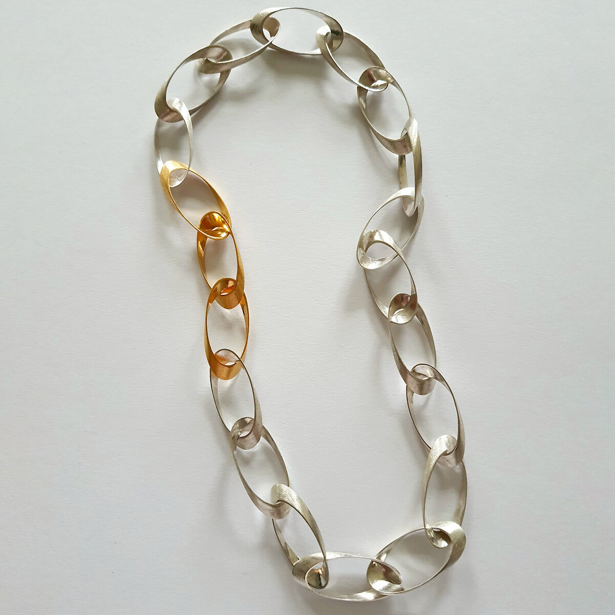 Edles Collier »Standing Ovations« der Marke HML Berlin aus 925er Silber und feingoldplattierten Elementen, bestehend aus handgefertigten ovalen Gliedern in Silber und Gold. Das Schmuckstück liegt auf hellem Untergrund und wirkt modern sowie puristisch.