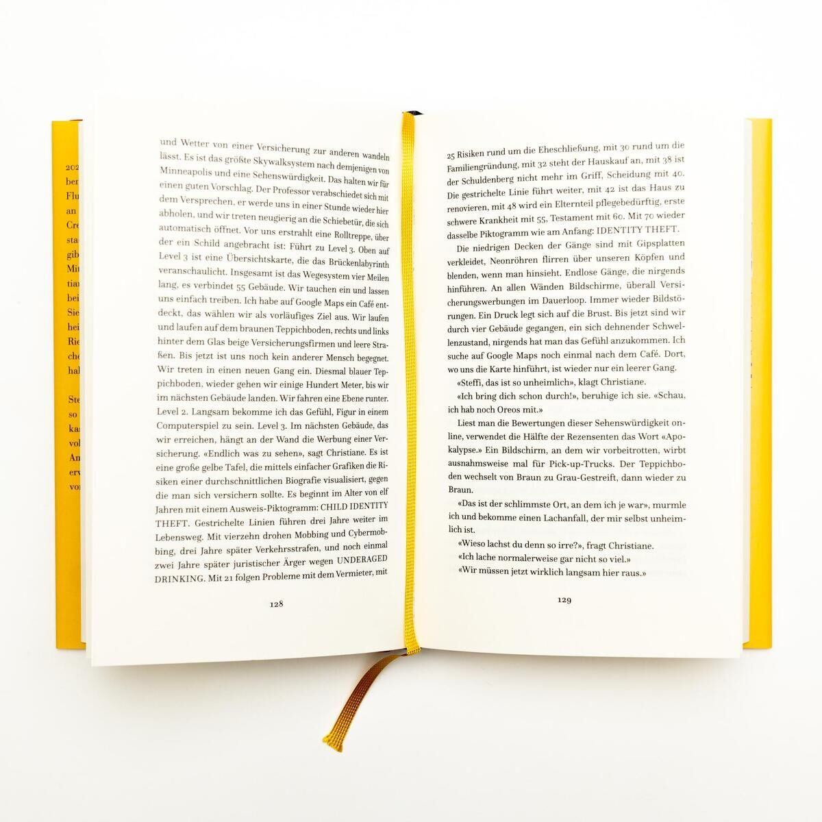 Offenes Buch von Sargnagel, betitelt 'Iowa', mit einem weißen Hintergrund. Das Buch zeigt Text auf Deutsch und hat ein gelbes Cover sowie ein braunes Lesezeichen.