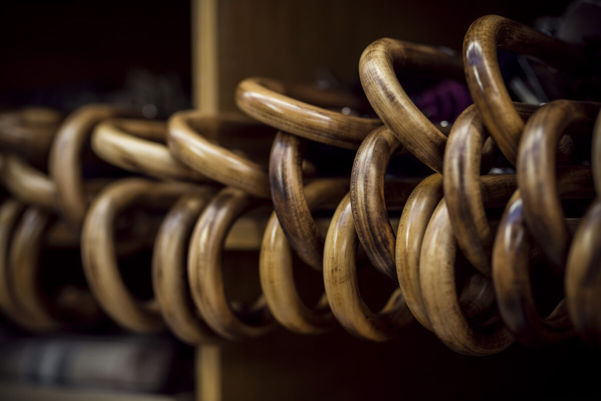 Nahaufnahme von braunen Holzringen, die in einem rustikalen Stil miteinander verschlungen sind. Es handelt sich um einen eleganten Schirm mit Ledergriff.