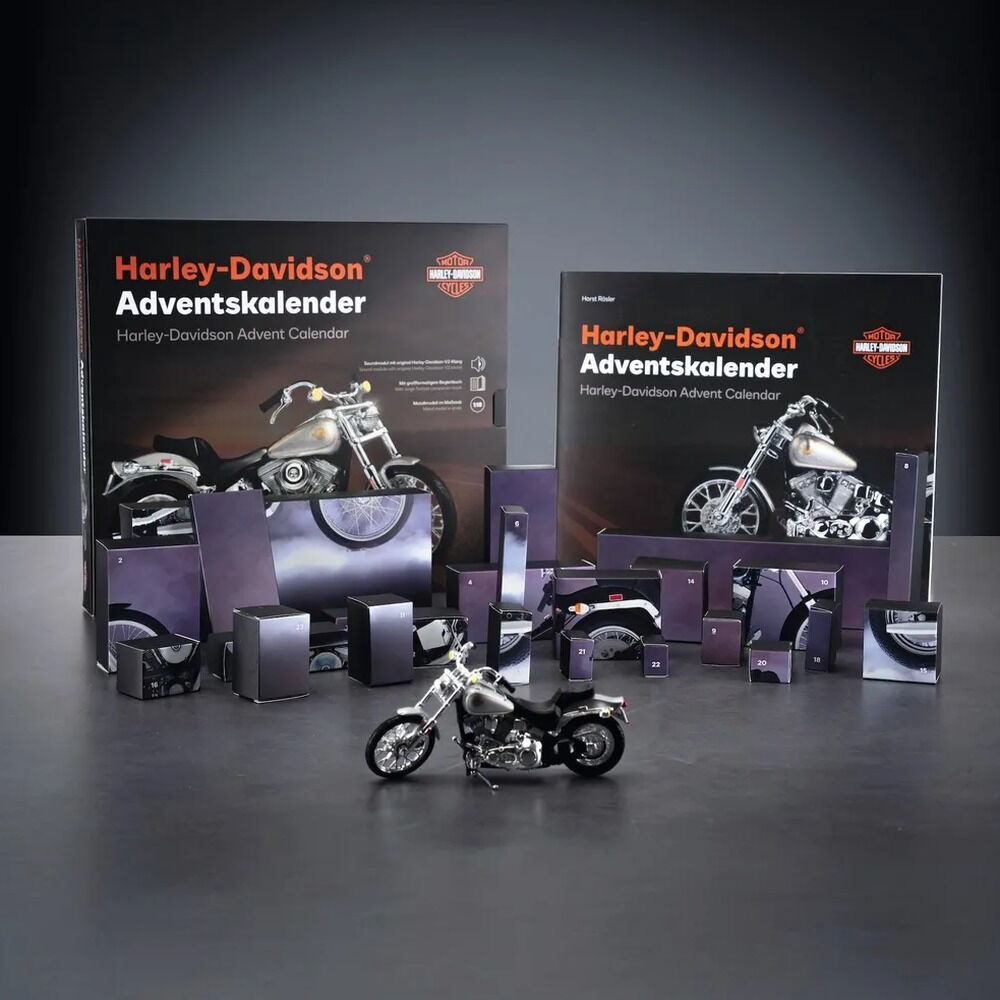 Produktaufbau des Harley-Davidson Adventskalenders: Zwei schwarze Schachteln mit orange-weißem Titel und Harley-Davidson-Logo zeigen ein silbernes Motorrad. Davor stehen zahlreiche dunkelviolett-schwarze, nummerierte Kalenderboxen, Teile und eine Soundbasis. Im Vordergrund steht das fertig montierte silber-schwarze Motorradmodell.