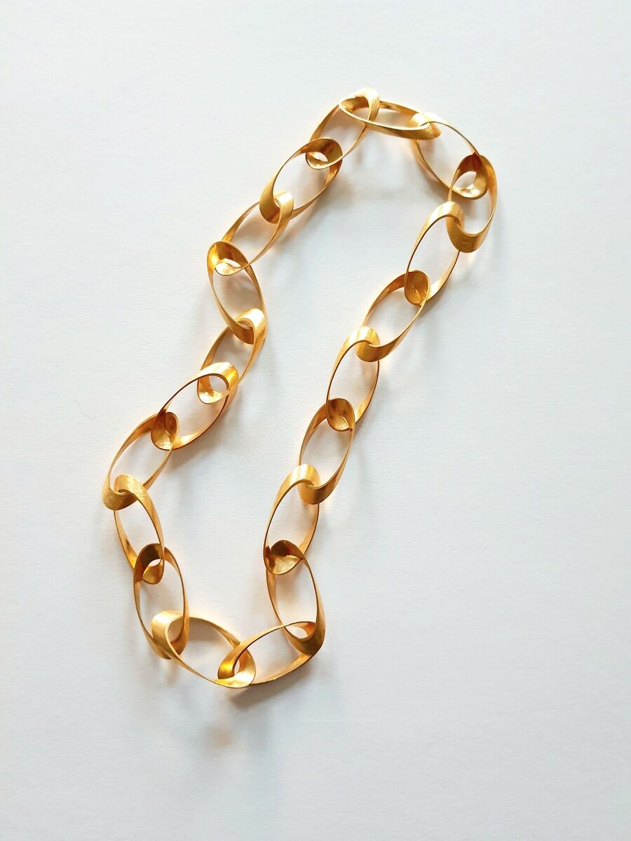 Dieses Bild zeigt ein elegantes, goldenes Collier mit ovalen Gliedern, das auf einer weißen Oberfläche liegt. Es betont Luxus und Stil.