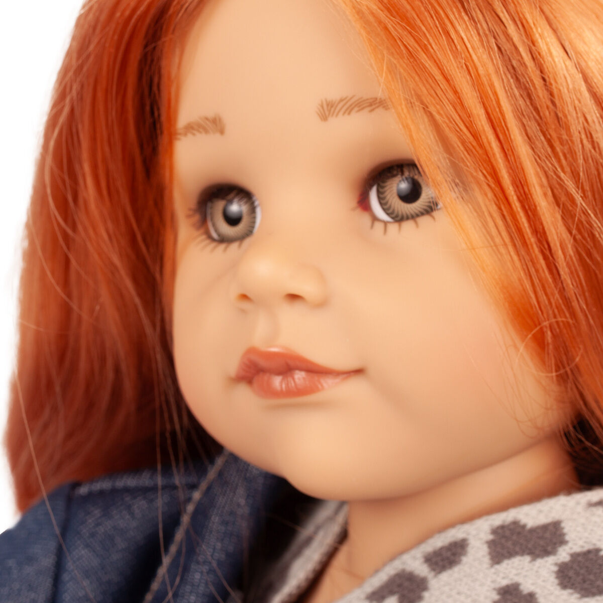 Großaufnahme einer Götz Stehpuppe „Hannah und ihr Hund Polly“ mit roten Haaren, blassem Teint, blaugrauen Augen, bekleidet mit einem grauen Oberteil mit Sternenmuster und einem blauen Stoff. Die Puppe wirkt realistisch und hochwertig gefertigt.