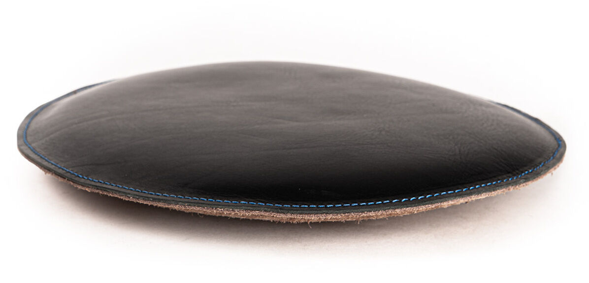 Das Bild zeigt ein rundes Sitzpolster aus schwarzem Leder der Marke Harold's Lederwaren. Das Polster liegt flach auf einer weißen Fläche und hat sichtbare braune Nähte am Rand. Es wirkt hochwertig verarbeitet und ist für Sitzkomfort gedacht.