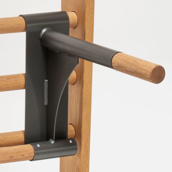 Detailansicht einer Sprossenwand aus Eiche mit einer schwarzen Metallhalterung für einen Trainingsgriff. Das hochwertige Holz ist naturfarben und zeigt eine helle, glatte Oberfläche. Die Konstruktion ist modern und minimalistisch gestaltet. Geeignet für Fitness und Bewegung in Wohnräumen oder Fitnessstudios.