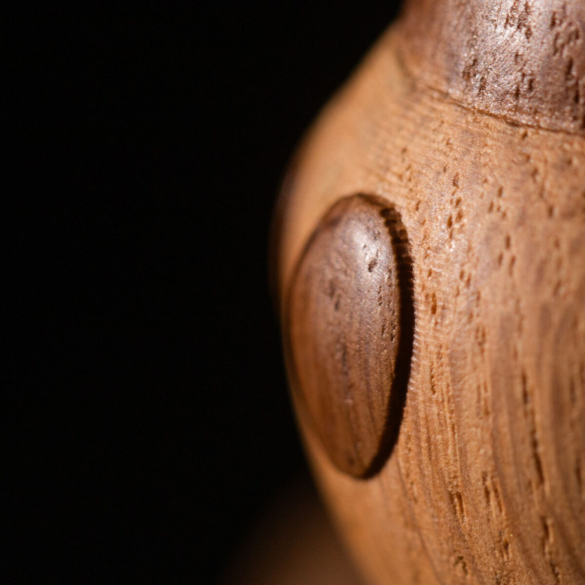 Detailaufnahme einer Holzfigur von Mickey Maus aus europäischer Eiche und rauchgebeizter Eiche von Boyhood. Sichtbar sind die runde Wange und das Ohr mit schöner Holzmaserung und glatter Oberfläche. Dezent inszeniertes Close-Up mit Disney-Logo auf dunklem Hintergrund.