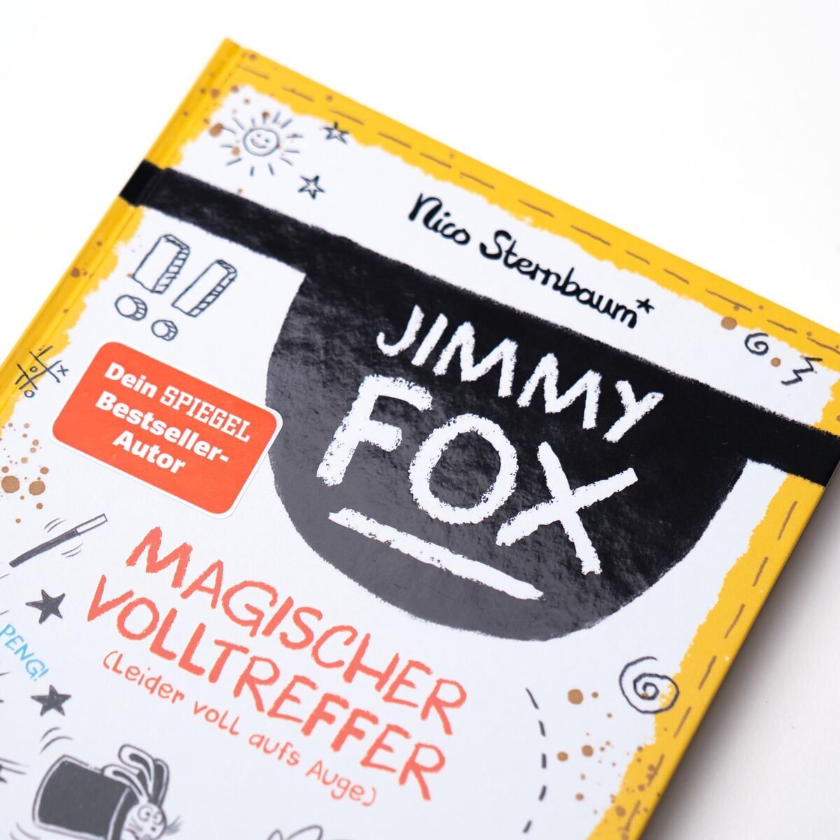 Buchcover von 'Jimmy Fox. Magischer Volltreffer' von Nico Sternbaum. Oben steht der Name des Autors. In der Mitte des Covers sind der Titel 'Jimmy Fox' in schwarzen und weißen Blockbuchstaben und der Untertitel 'Magischer Volltreffer (Leider voll aufs Auge)'. Es gibt auch einen orangefarbenen Aufkleber mit der Aufschrift 'Dein SPIEGEL Bestseller Autor'. Die Abdeckung ist mit kleinen Zeichnungen und Symbolen in Schwarz und Orange verziert.
