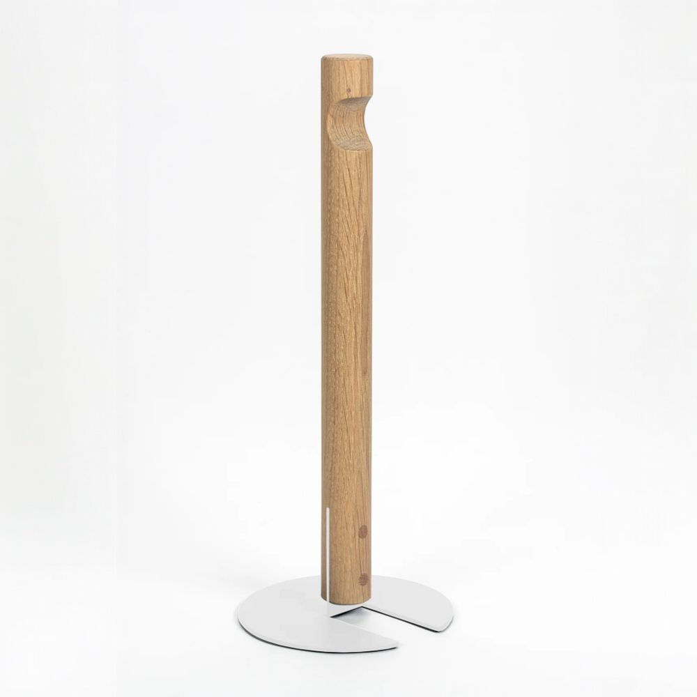 Freistehender Küchenrollenhalter GIVE von finbeaux vor weißem Studiohintergrund. Ein hoher, schlanker Stab aus hellbraunem Holz mit sichtbarer Maserung und einer ausgearbeiteten Griffmulde oben steht auf einem flachen, silberfarbenen Metallfuß mit zwei abgerundeten, geschlitzten Flügeln.