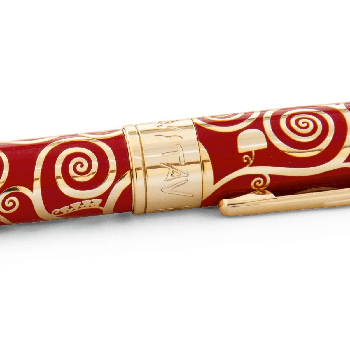 Detailaufnahme eines edlen Kugelschreibers aus Metall mit rotem Hintergrund und goldenen, kunstvollen Ornamenten im Stil von Gustav Klimts "Baum des Lebens". Der Clip und der Mittelring sind goldfarben, der Schaft ist mit dekorativen Spiralmotiven verziert.