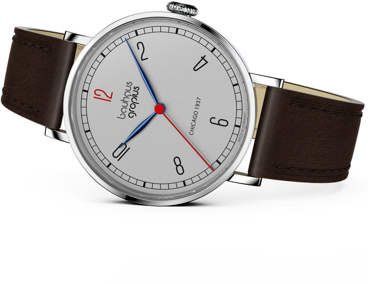 Hochwertige Armbanduhr der ZEIT-Sonderedition Walter Gropius »New Bauhaus Chicago 1937« mit silberfarbenem Gehäuse, weißem Zifferblatt und minimalistischen Zahlen. Die Zeiger sind in Blau, Rot und Schwarz gehalten. Das Armband ist braun und aus Leder.