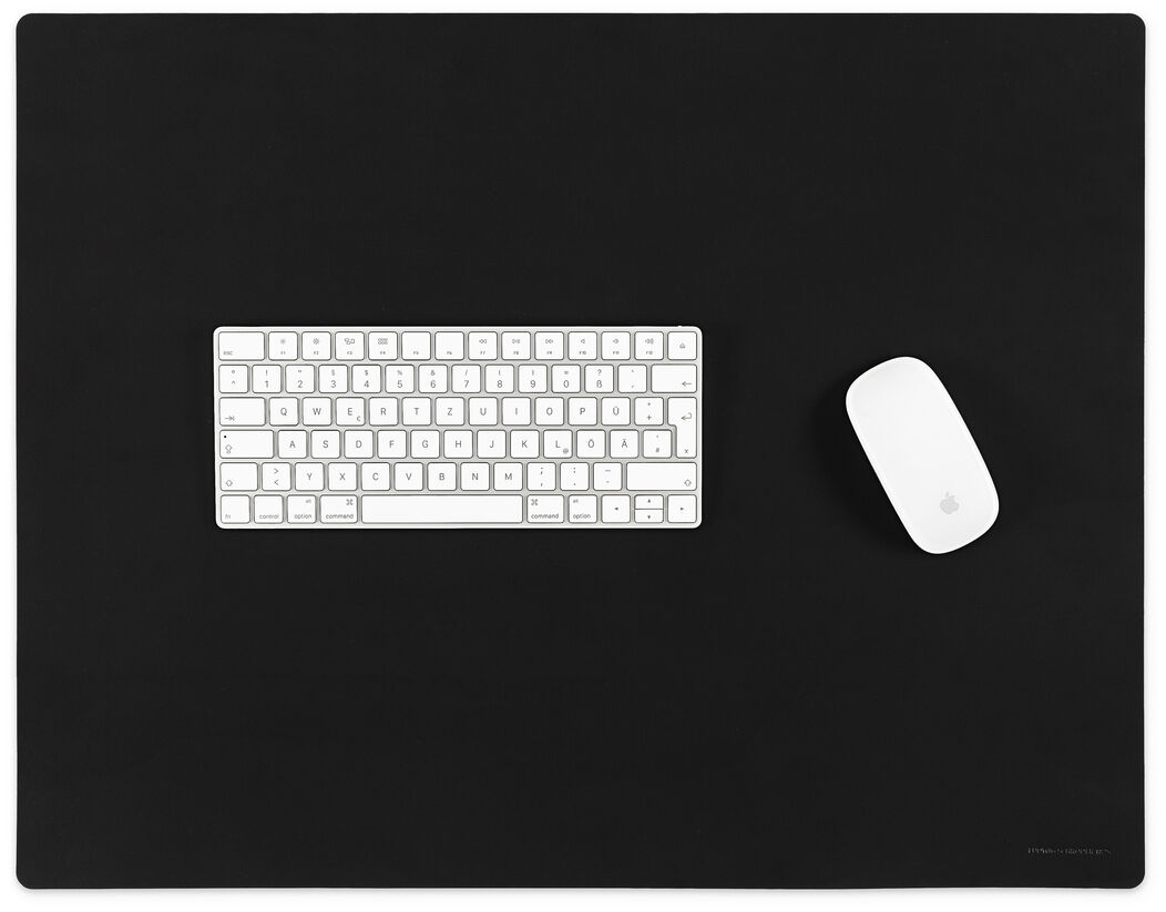 Eine schwarze Schreibtischunterlage mit darauf platzierter weißer Tastatur und Computermaus. Minimalistisches und elegantes Design.