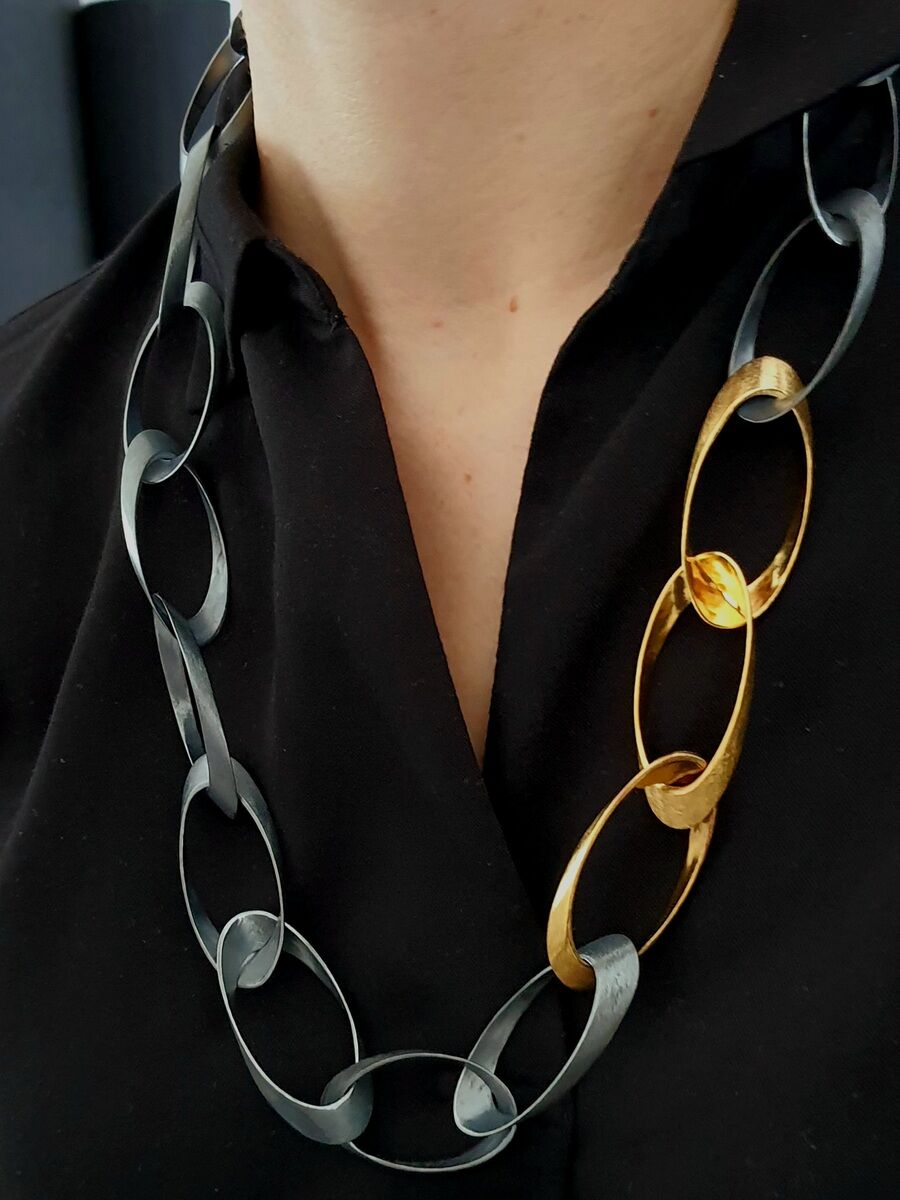 Silberne und goldene Halskette mit ovalen Kettengliedern, getragen von einer Person in schwarzer Kleidung.