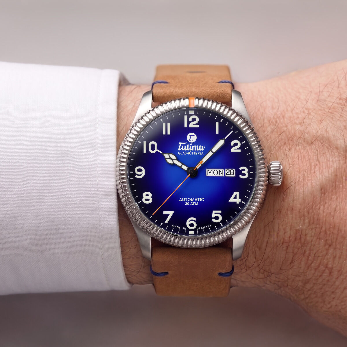 Die Tutima Glashütte ZEIT-Sonderedition "Grand Flieger Classic Automatic" mit tiefblauem Zifferblatt, silbernem Edelstahlgehäuse und hellbraunem Lederarmband sitzt am Handgelenk eines Mannes mit weißem Hemd. Sichtbar sind Zahlen, Wochentag und Datum.