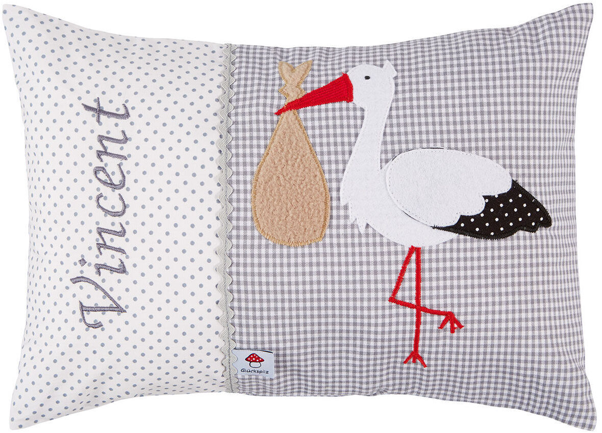 Namenskissen mit personalisiertem Namen »Vincent«, zeigt einen weißen Storch mit rotem Schnabel und Beinen, der eine beige Tasche trägt, auf einem Hintergrund aus weiß gepunktetem und grauem Karomuster.