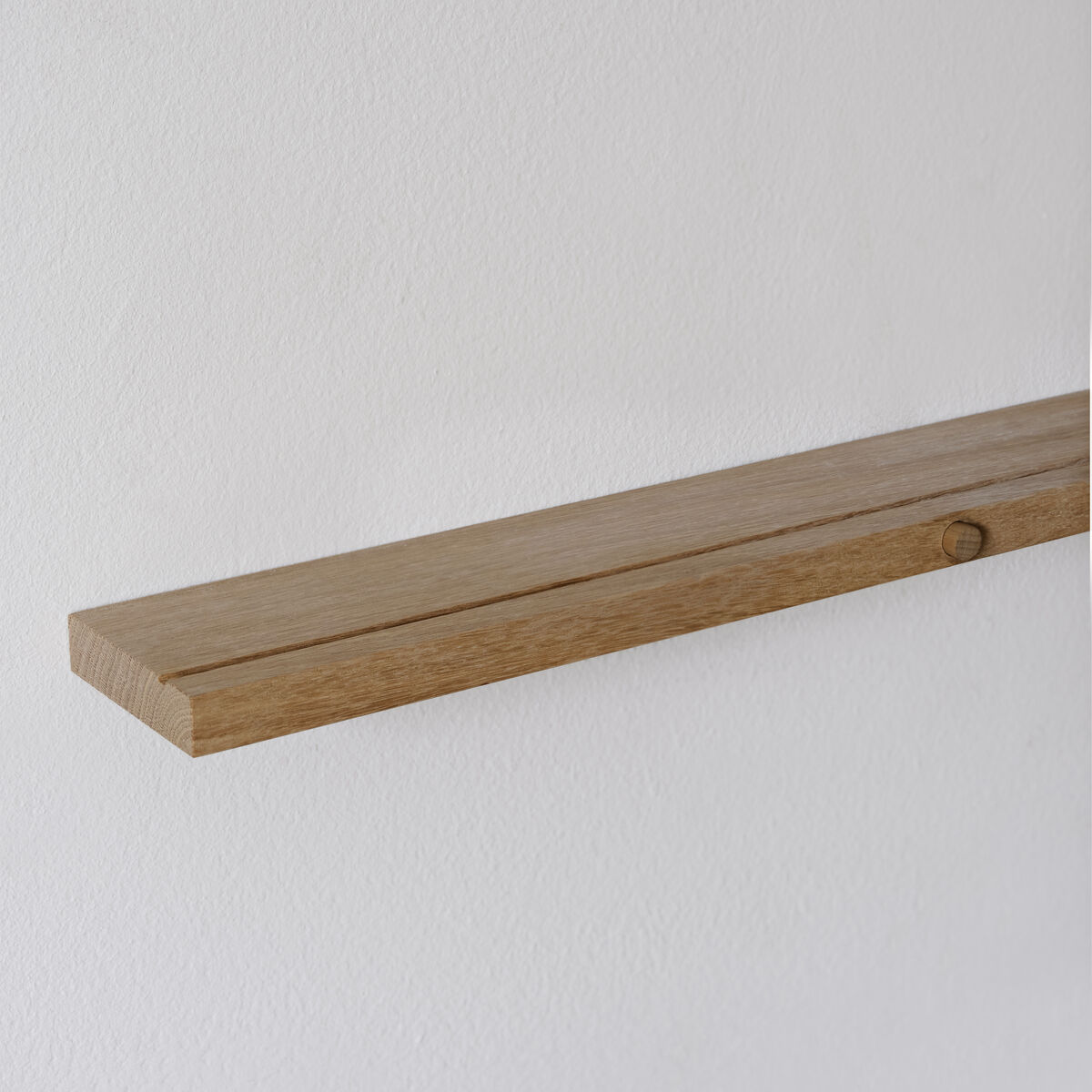 Ein schlichtes, wandhängendes Regal aus Eichenholz vor einer weißen Wand.