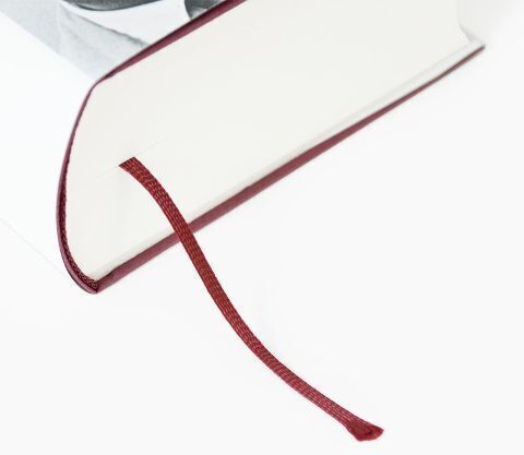 Nahaufnahme eines Buches mit weißem Einband und dunkelroter Lesezeichen-Schleife.