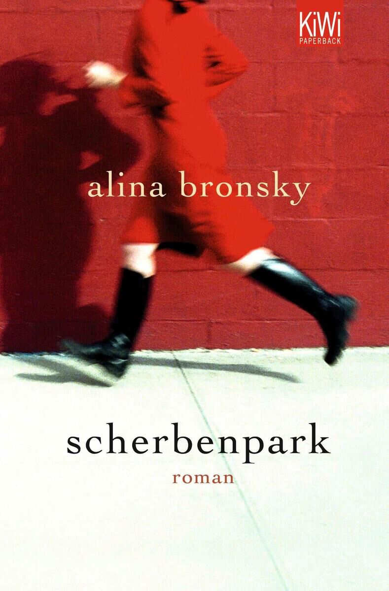 Das Cover des Buches 'Scherbenpark' von Alina Bronsky zeigt eine Person in einem roten Mantel, die vor einer roten Wand entlangläuft. Der Titel steht in weißen Buchstaben auf einem weißen Boden, während der Name der Autorin in gelben Buchstaben auf der roten Wand darüber zu sehen ist.