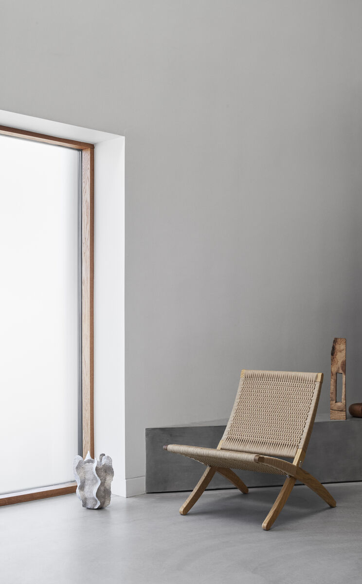 Das Bild zeigt den »MG501 Cuba Chair«, ein moderner Stuhl im minimalistischen Design mit Rattanelementen und Holzstruktur. Der Stuhl ist neben einem großen Fenster in einem hellen Raum platziert, mit weiteren Dekorationsgegenständen im Hintergrund.
