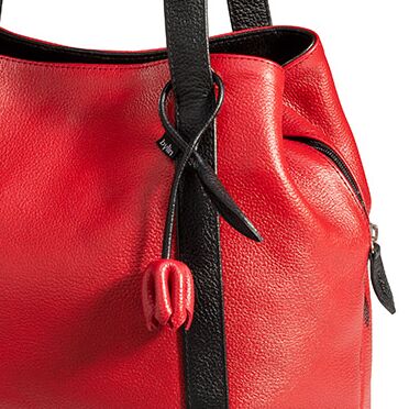 Detailansicht eines eleganten Shoppers aus rotem Leder mit schwarzen Lederhenkeln. Ein dekoratives, schwarzes Lederband endet in einer roten Tulpenapplikation. Seitlich sichtbarer Reißverschluss, fein strukturierte Lederoberfläche, modernes Design.