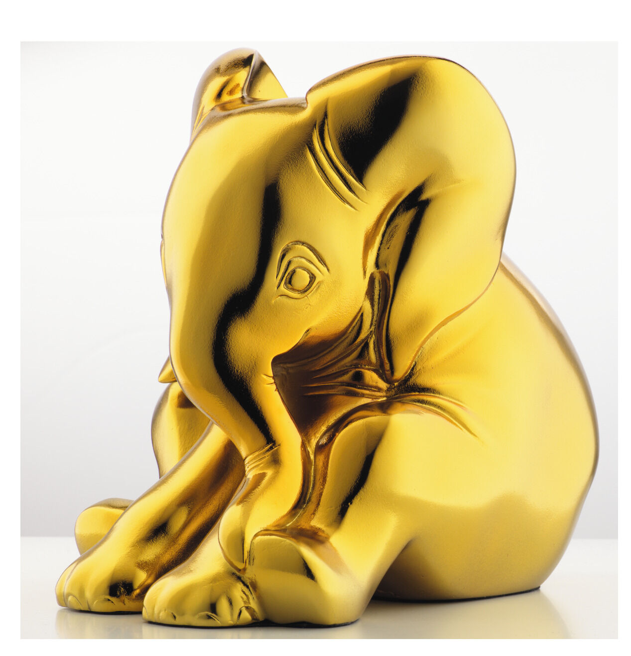 Eine goldene Elefantenskulptur, die aus Kunstguss gefertigt wurde. Der Elefant ist detailliert gestaltet und sitzt aufrecht. Das Bild zeigt die Skulptur vor einem hellen, neutralen Hintergrund.