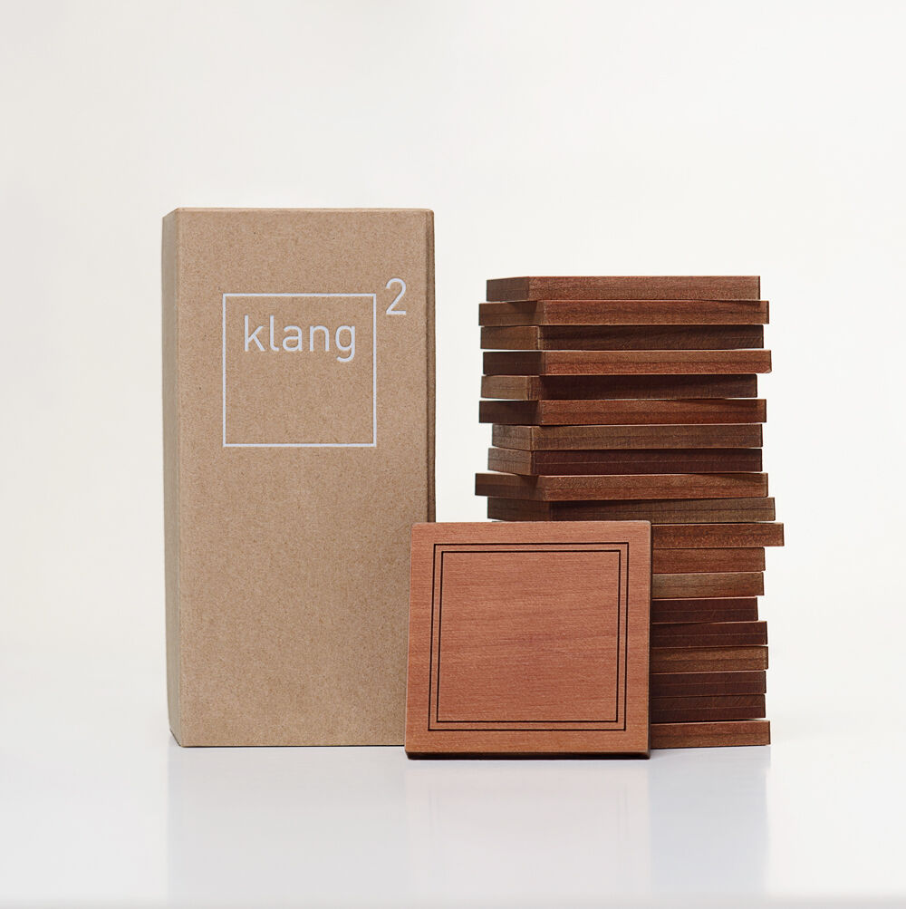 Bild der Klang² Spielesammlung »Geigenbauer«, bestehend aus mehreren gestapelten Holzblöcken und einer beigen Verpackung mit dem Logo klang² darauf.