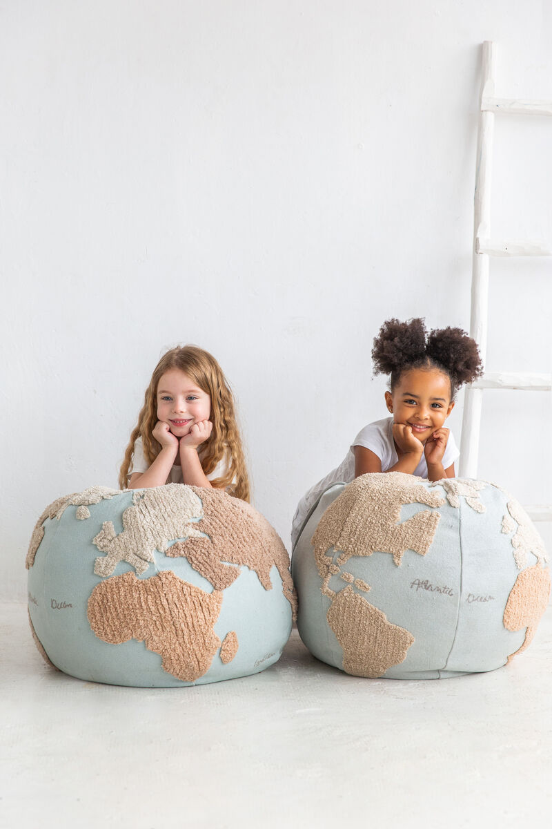Zwei Kinder sitzen auf runden Sitzkissen mit Weltkartenmuster. Die Kissen sind in Beige und Blau gehalten. Die Kinder scheinen glücklich und bequem zu sein.