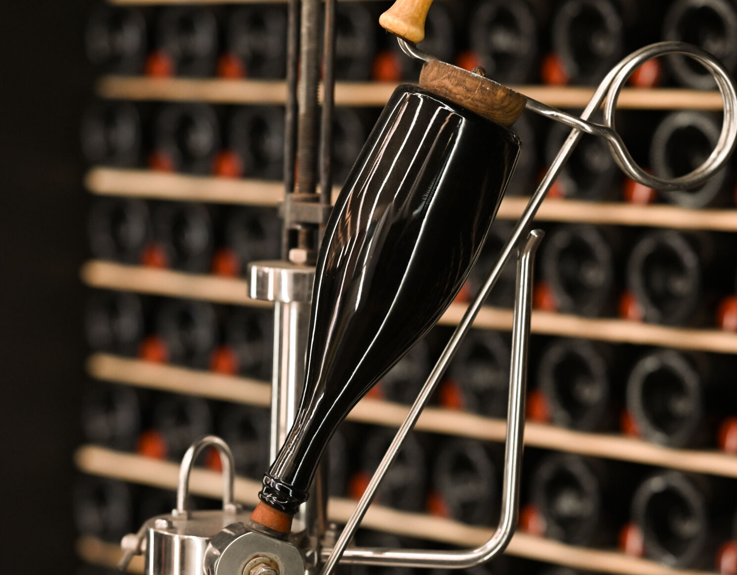 Flaschenverschlussmaschine mit einer eingespannten Weinflasche vor einem Regal mit vielen Weinflaschen.