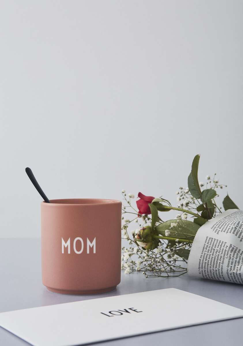 Ein rosafarbener Becher mit der Aufschrift 'MOM', daneben eine weiße Karte mit dem Wort 'LOVE' und einige Blumen.