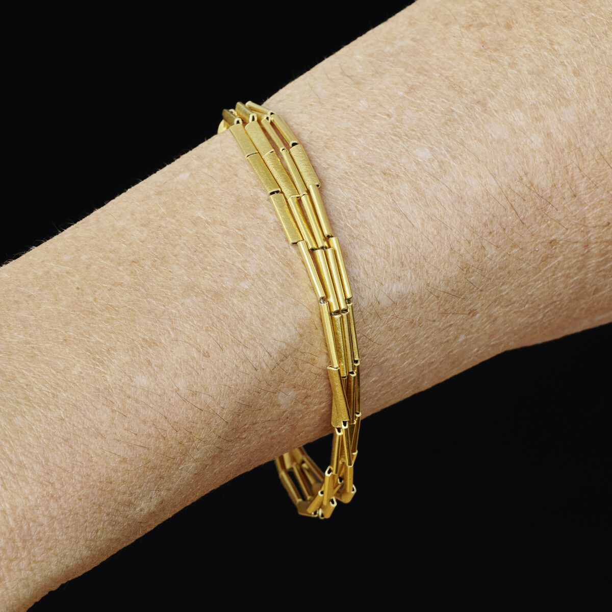 Schlankes Halmarmband aus Silber, feingoldplattiert, getragen am Handgelenk vor schwarzem Hintergrund. Das Armband wirkt elegant und filigran, ideal als feines Schmuckstück für festliche und persönliche Anlässe.