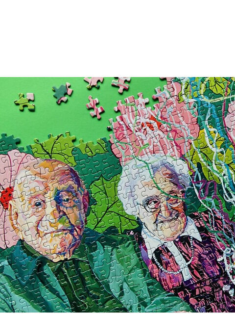 Ein farbenfrohes Puzzle mit dem Motiv »It's never Too Late to Celebrate«, das zwei ältere Personen zeigt, umgeben von Blumen und Luftballons auf grünem Hintergrund.