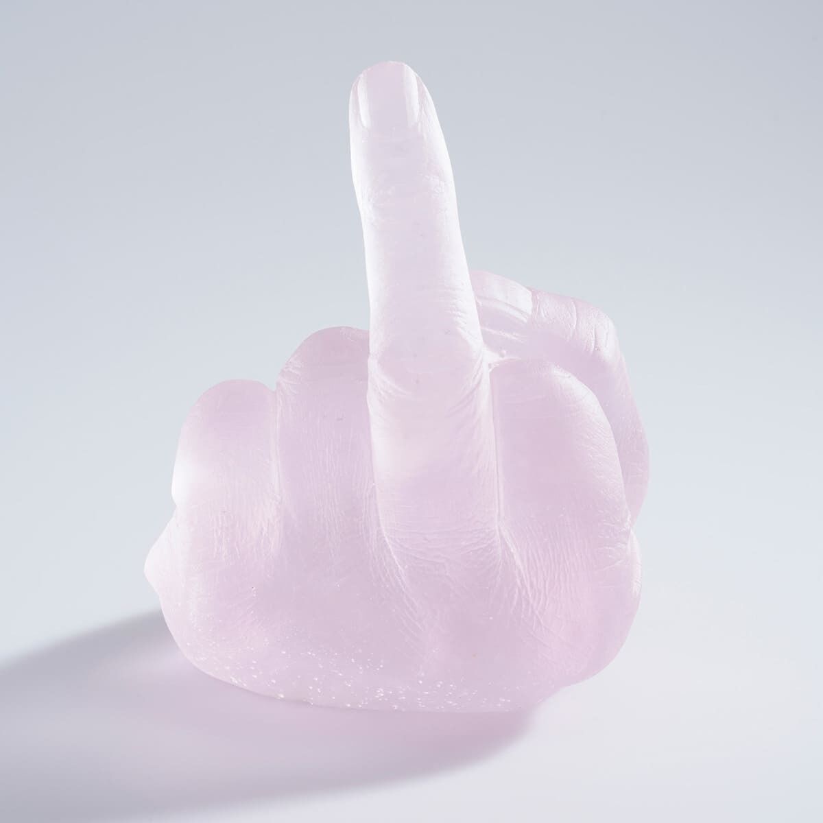 Eine Skulptur aus Glas von Ai Weiwei mit dem Titel »Study of Perspective in Glass«, die eine Hand darstellt, die den Mittelfinger hochhält. Die Skulptur ist in einem transparenten Rosa-Ton gehalten und vor einem neutralen Hintergrund fotografiert.