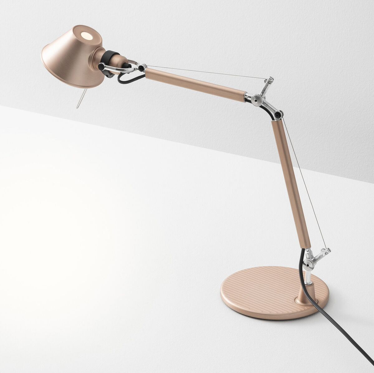 Eine minimalistische Tischlampe von Artemide, Modell ‚Tolomeo Micro‘, in Weiß und Silber mit einem verstellbaren Schwenkarm auf einem weißen Tisch.