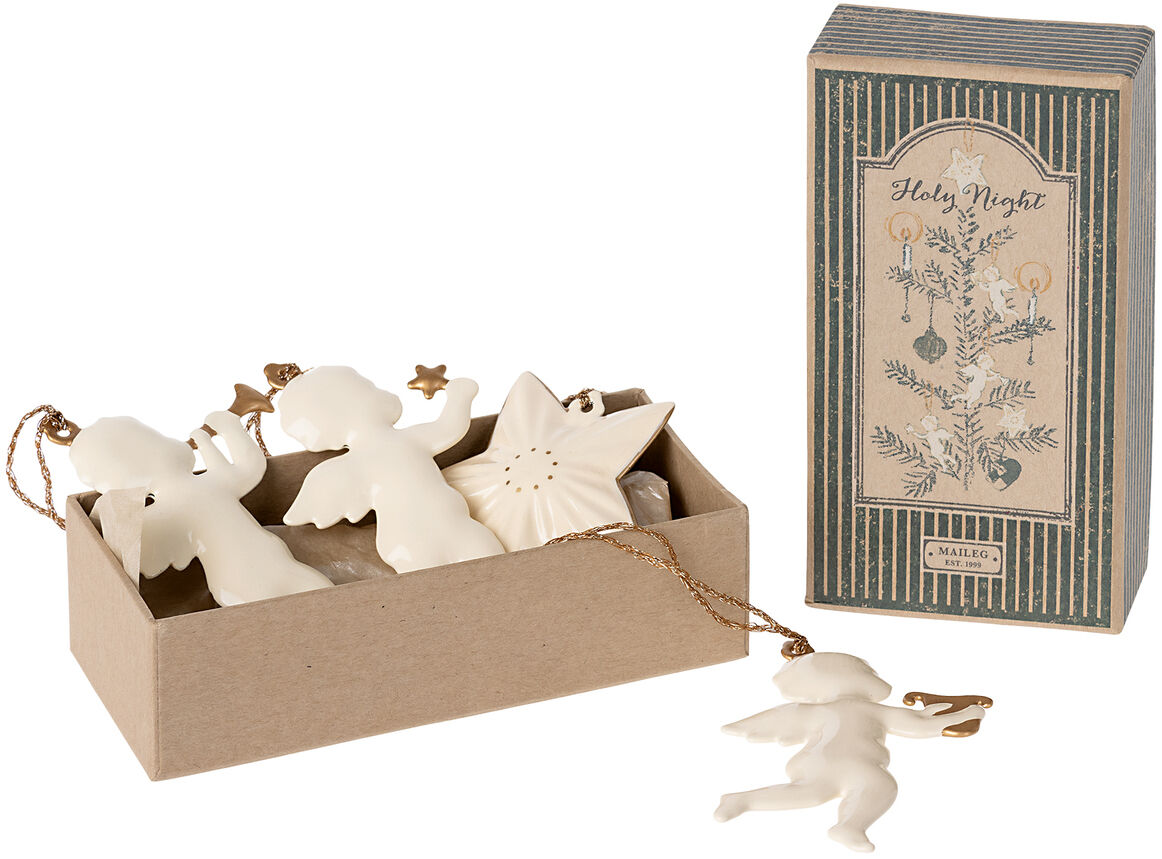 Ein Set von Weihnachtsanhängern mit Figuren eines Engels und eines Sterns in einer rechteckigen Schachtel neben einer dekorativen Verpackung mit der Aufschrift „Heilige Nacht“.