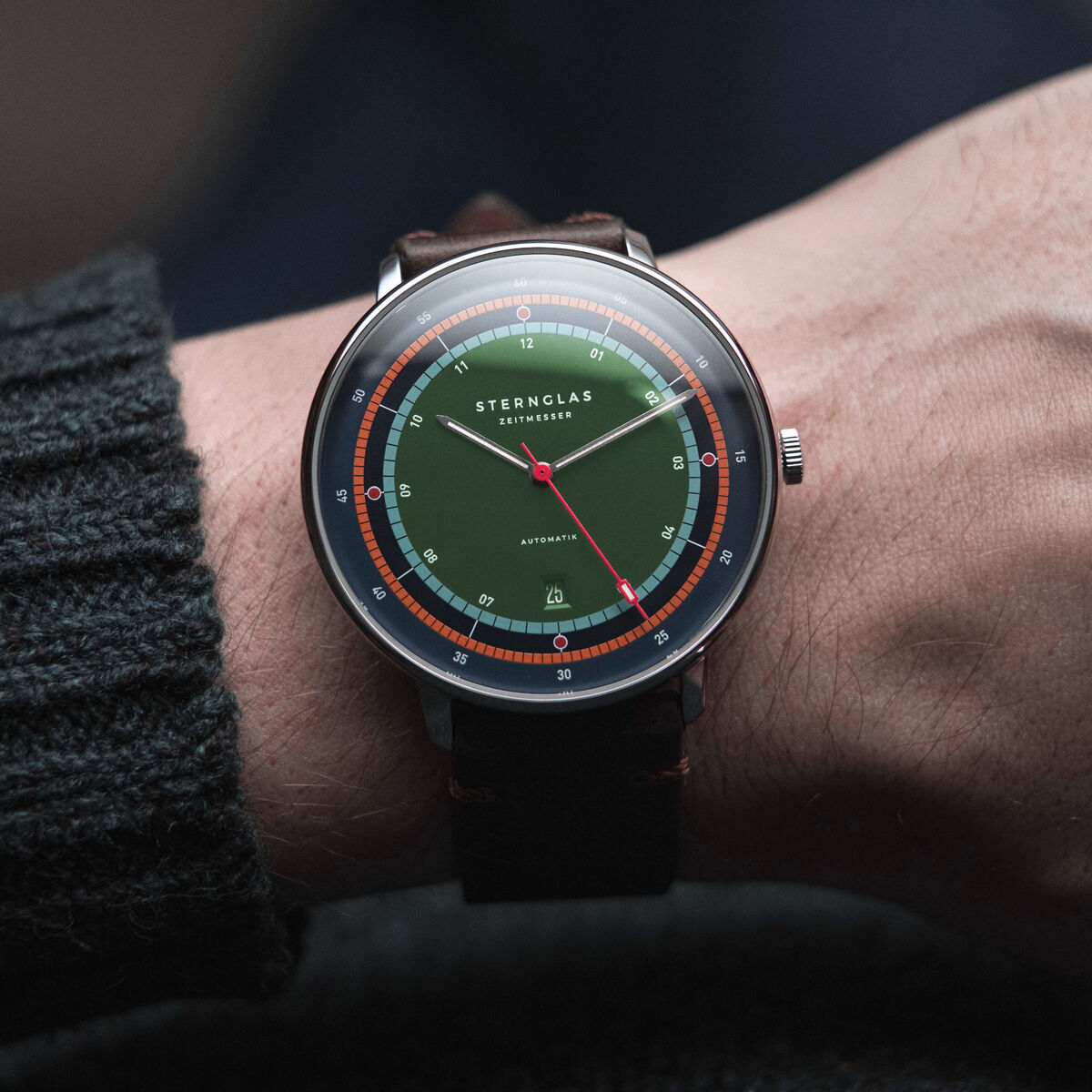 Die ZEIT-Sonderedition Uhr 'Hamburg Automatic' zeigt ein elegantes Design mit einem grün-blauen Zifferblatt und einem braunen Lederarmband. Die Uhr hat ein minimalistisches Zifferblatt mit orangefarbenen und silbernen Details.