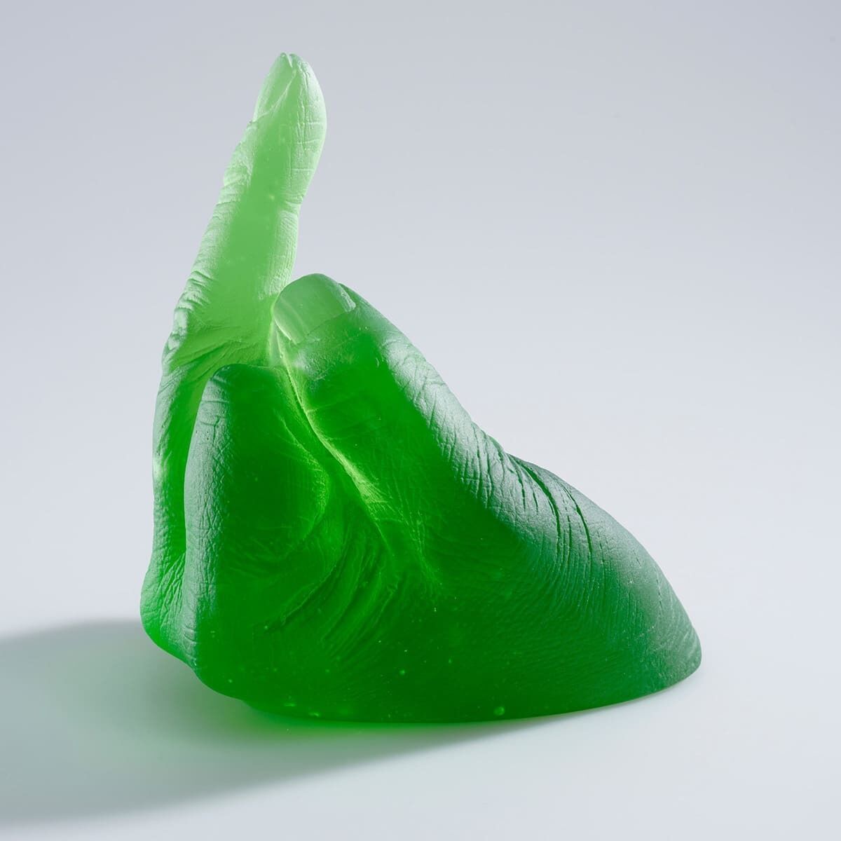 Eine grüne, durchsichtige Skulptur von Ai Weiwei mit dem Titel »Study of Perspective in Glass«. Sie zeigt eine Hand mit ausgestrecktem Mittelfinger. Die Skulptur hat eine detaillierte Textur und steht auf einer weißen Oberfläche.