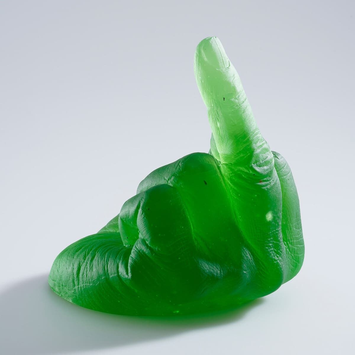 Eine grüne Skulptur aus Glas, die eine Hand darstellt, die den Mittelfinger zeigt. Sie steht auf einem weißen Hintergrund.