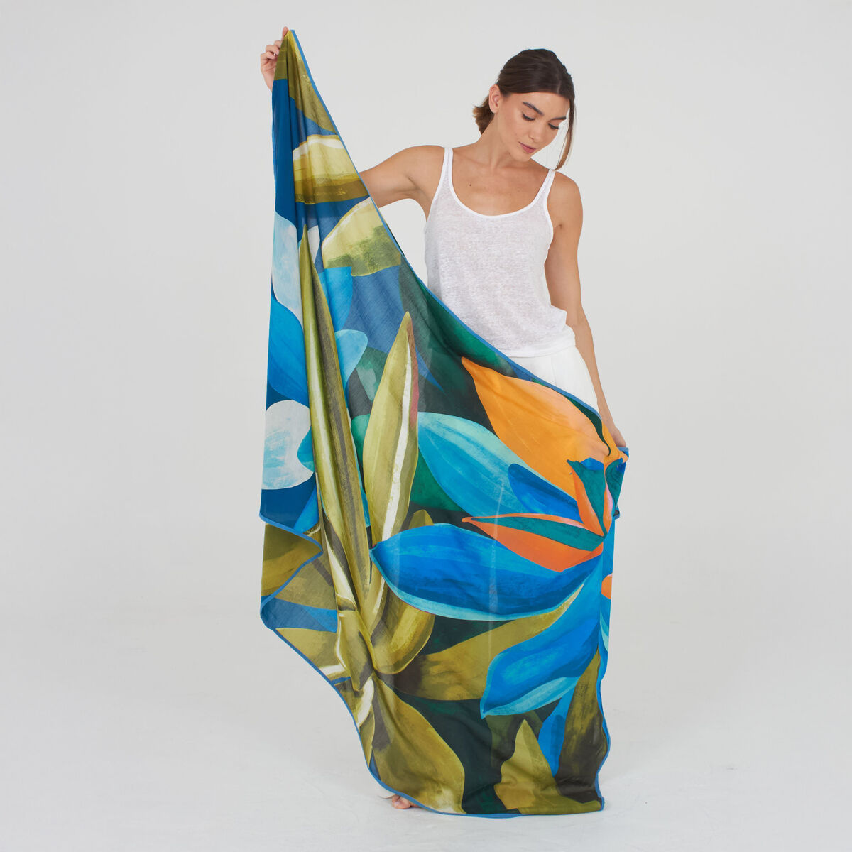 Ein eleganter Baumwoll-Seidenschal »Cassey« der Marke Shalls Barcelona liegt locker drapiert. Der Schal zeigt leichte, aquarellartige Übergänge in Blau, Grün und Türkis auf weißem Grund. Der Stoff wirkt leicht, hochwertig und fließend, geeignet für modebewusste Frauen.