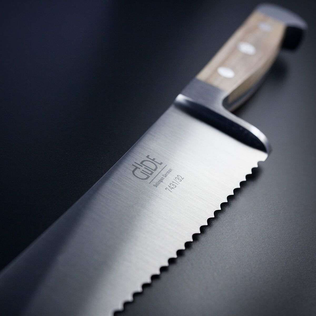 Ein hochwertiges Brotmesser mit gezackter Edelstahlklinge und stabilem Holzgriff liegt auf einer dunklen Unterlage. Das Messer ist teilweise glänzend und ideal zum Schneiden von Brot geeignet.