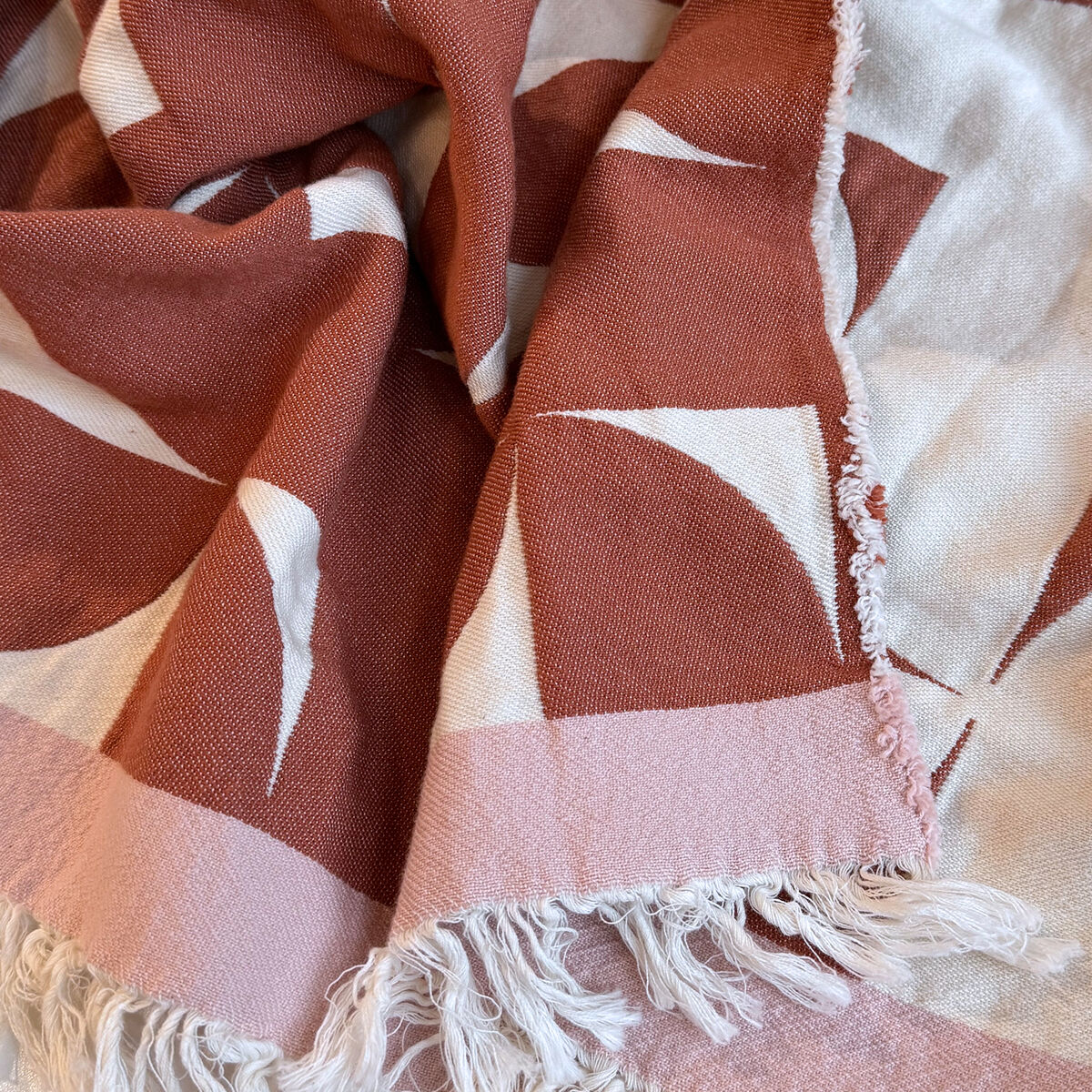 Baumwolldecke mit modernem skandinavischen Design, in Weiß und Rosa mit geometrischen Mustern. Die Decke wirkt weich und gemütlich, perfekt für das Wohnzimmer.