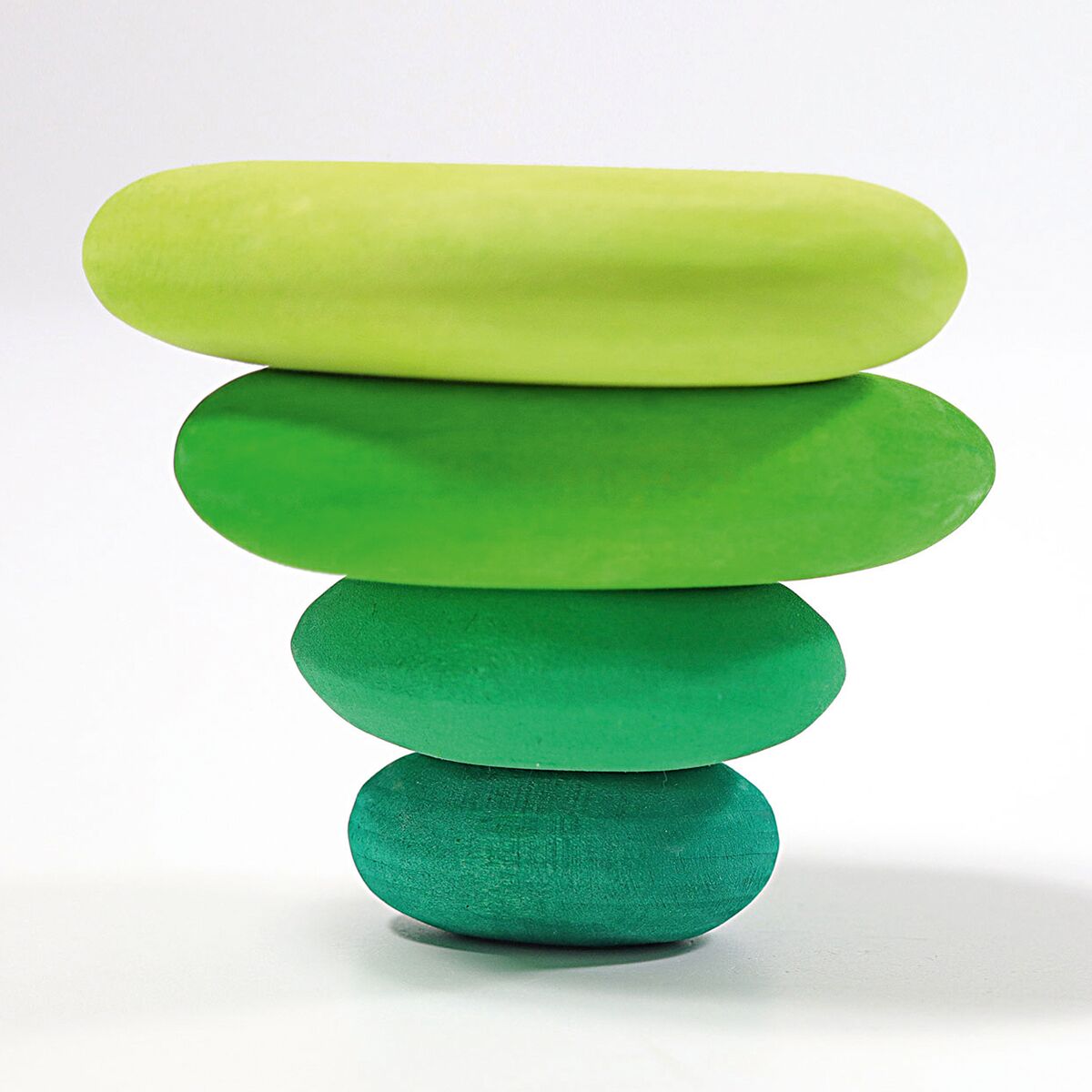 Vier unterschiedlich große, farbig lasierte Holzsteine in limetten- bis dunkelgrünen Farbtönen, balancierend aufeinander gestapelt. Die Steine wirken glatt, organisch geformt und liegen auf einer weißen, ebenen Fläche. Kein weiteres Zubehör oder Dekoration erkennbar.