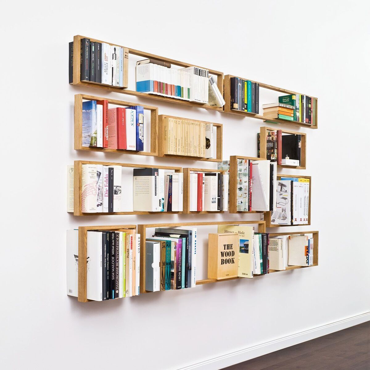 Ein großes, an der Wand montiertes Regal aus Holz mit mehreren Fächern, gefüllt mit verschiedenen Büchern und Zeitschriften. Das Regal hat ein minimalistisches Design in den Farben Weiß und Braun.