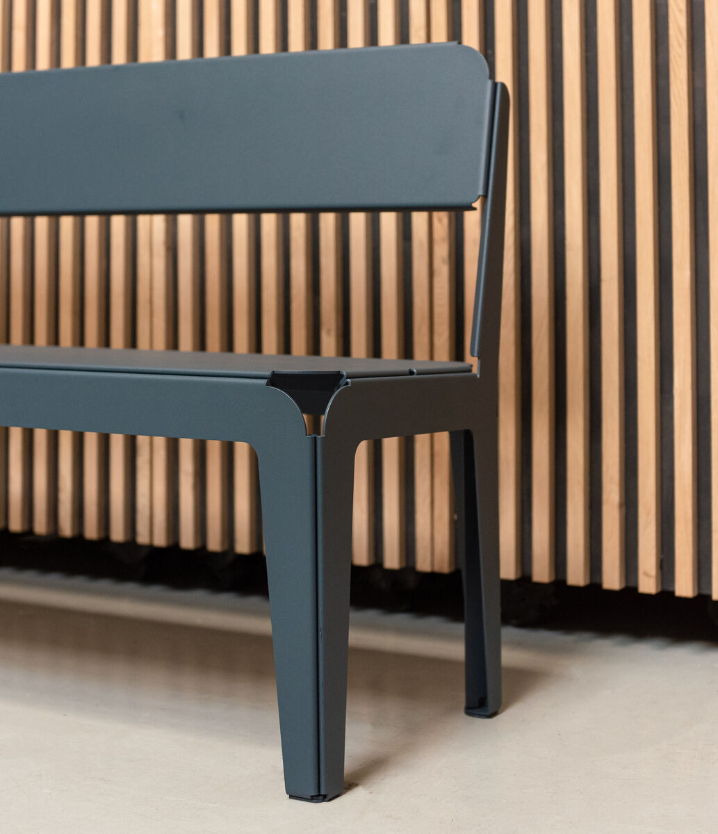 Eine stilvolle Bank mit Rückenlehne aus Metall in grauer Farbe steht vor einer vertikalen Holzverkleidung. Das Design ist modern und minimalistisch, ideal für Außenbereiche und stilvolle Gartengestaltung.