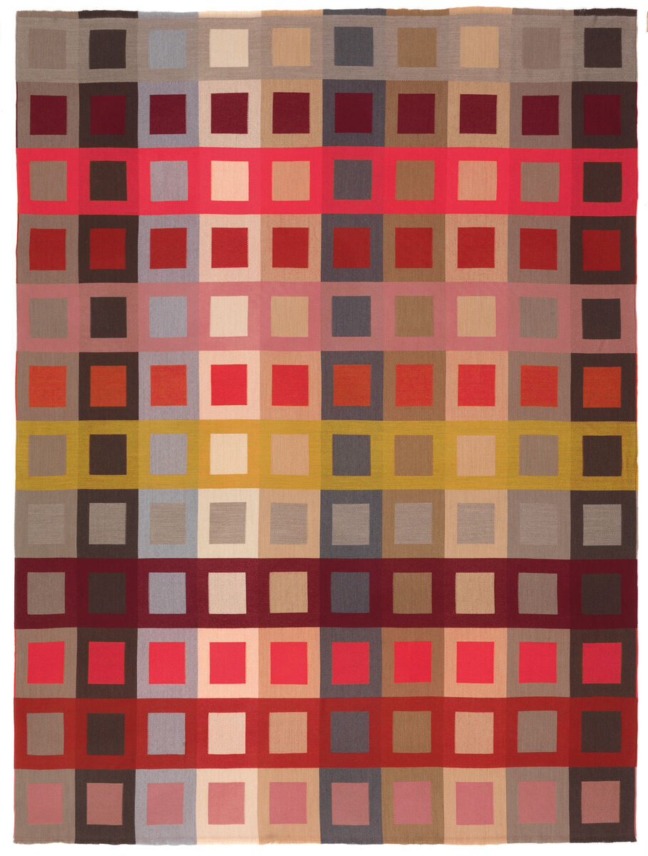 Eine Decke mit einem geometrischen Muster aus vielen verschiedenfarbigen Quadraten, vorwiegend in Rot-, Grau-, Gelb-, Rosa-, Braun- und Beigetönen.