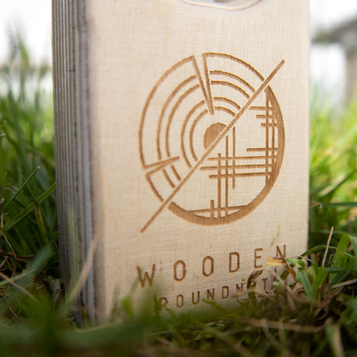 Nahaufnahme eines Wooden Roundnet-Sets auf grünem Gras. Der Holzrahmen zeigt ein rundes Muster und die eingravierte Aufschrift 'Wooden Roundnet'.