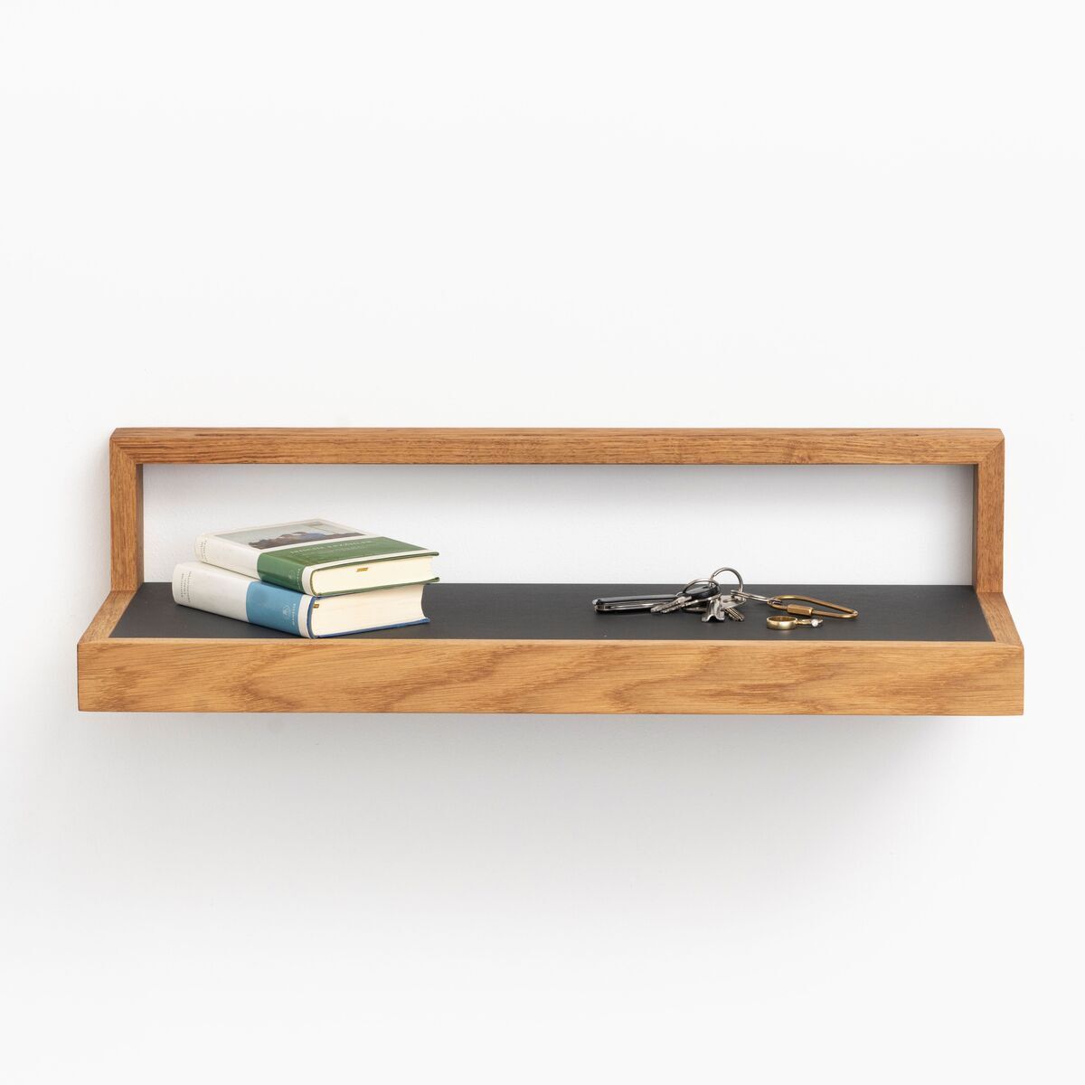 Ein Ablagebord in der Farbe Anthrazit mit einer Einfassung aus hellem Holz ist an einer weißen Wand montiert. Auf dem Bord liegen zwei Bücher und ein Schlüsselbund.