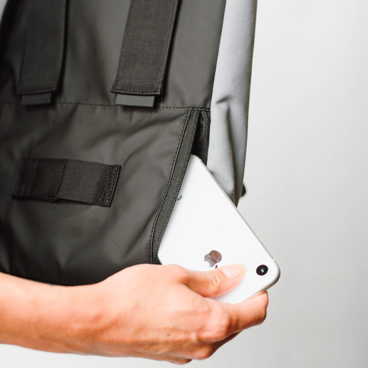 Nahaufnahme einer Fahrradtasche/Rucksack »Annecy«, die schwarze und graue Farben zeigt. Eine Hand steckt ein Smartphone in die Tasche.
